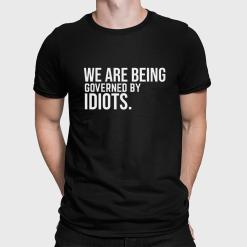 A man wearing a black shirt that says we are being governed by idiots.