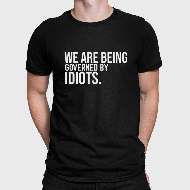 A man wearing a black shirt that says we are being governed by idiots.